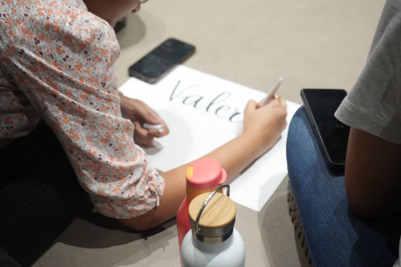 A hand writes the word Value in large letters on a sheet of paper.