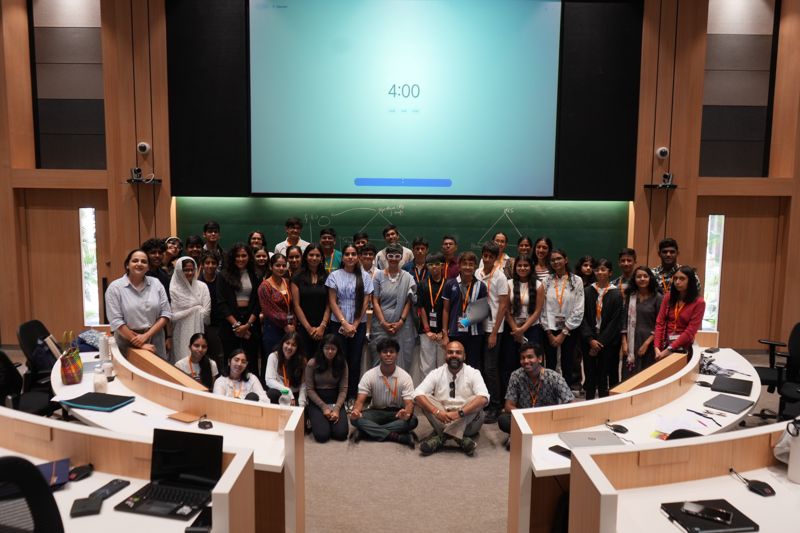 The whole cohort together in a lecture theatre, some standing and some sitting on the floor in front.